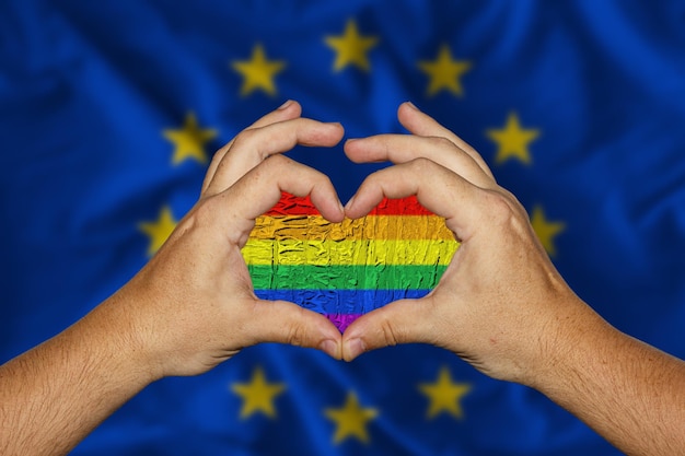 Mannelijke handen vormen een hart met een LGBT-vlag erin tegen de achtergrond Vlag van Europa