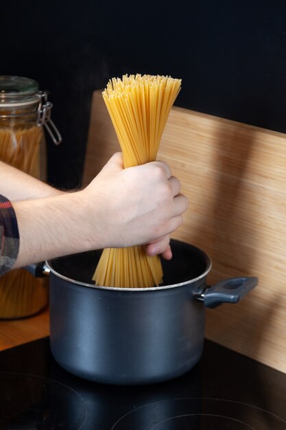 Mannelijke handen zetten een bos pasta in de kookpan,