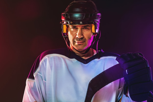 Mannelijke hockeyspeler met de stick op ijsbaan en donkere neon gekleurde muur