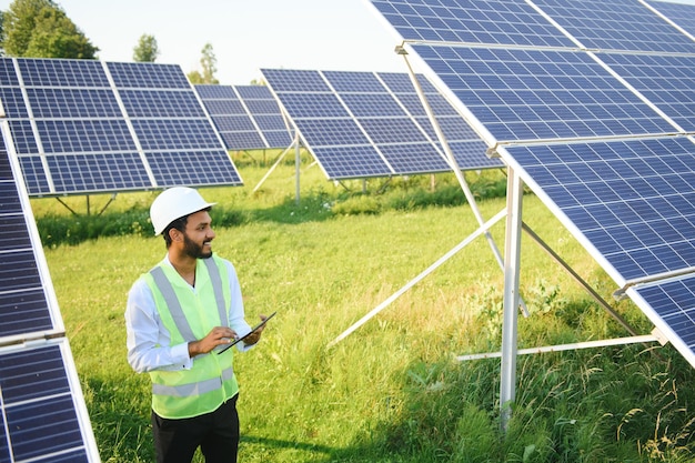 mannelijke ingenieur controleert een fotovoltaïsche zonne-energie-installatie en gebruikt een opname tablet Indiase man in uniform die tablet vasthoudt