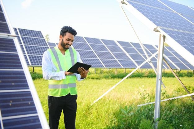 mannelijke ingenieur controleert een fotovoltaïsche zonne-energiecentrale en gebruikt een opnametablet Indiase man in uniform met tablet