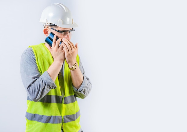 Mannelijke ingenieur die in het geheim aan de telefoon praat, geïsoleerd jonge ingenieur met helm die in stilte aan de telefoon spreekt en zijn mond bedekt.