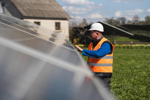 Mannelijke ingenieur in een helm en reflecterend vest inspecteert panelen bij zonne-energiecentrale