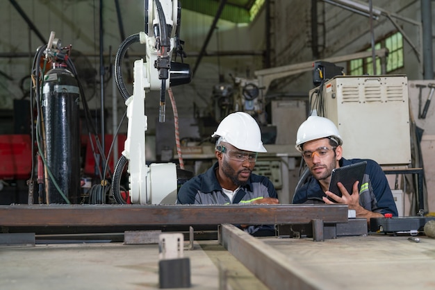 Mannelijke ingenieurs kijken naar las op staal dat wordt gelast door een robotarmmachine in de fabriekswerkplaats