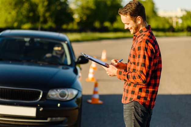 Mannelijke instructeur en vrouw in auto, verkeerskegels, les in rijschool. Man die dame leert voertuig te besturen. Rijbewijs opleiding