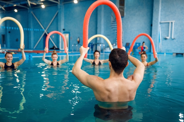 Mannelijke instructeur en vrouwelijke groep, aqua-aerobicstraining in het zwembad