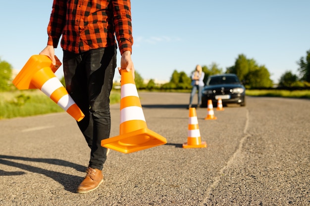 Mannelijke instructeur zet verkeerskegels op de weg, rijschool. Man die dame leert voertuig te besturen. Rijbewijs opleiding