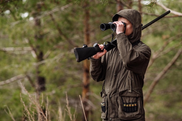 Mannelijke jager met verrekijker klaar om te jagen met pistool en wandelen in het bos