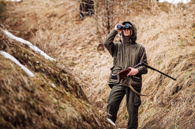Mannelijke jager met verrekijker klaar om te jagen met pistool en wandelen in het bos