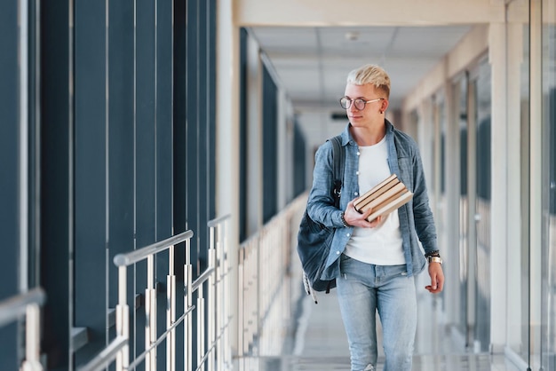 Mannelijke jonge student in jeanskleding is in de gang van een universiteit met boeken in handen