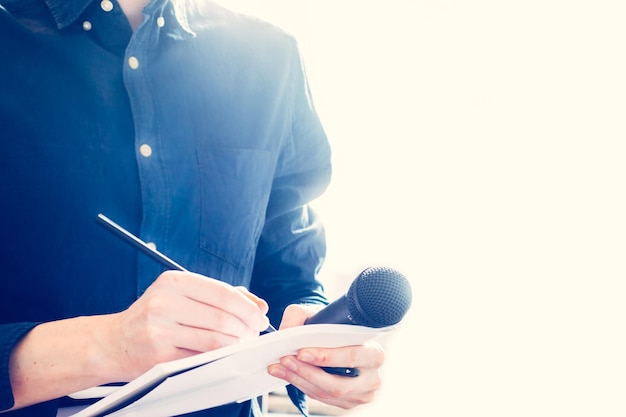 Mannelijke journalist op persconferentie die microfoon vasthoudt en aantekeningen maakt