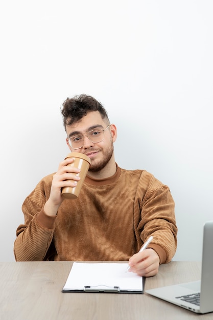 Mannelijke kantoormedewerker zittend aan een bureau met een kopje koffie en het maken van aantekeningen.