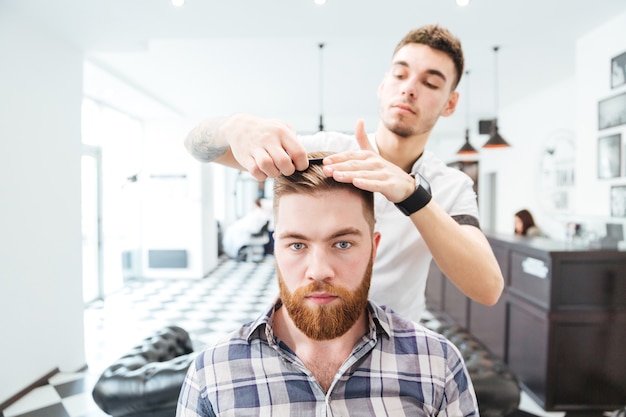 Mannelijke kapper die haar kamt aan zijn cliënt in herenkapper