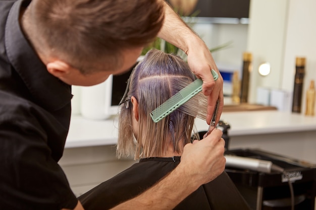 Mannelijke kapper die vrouwenhaar knippen met professionele schaar