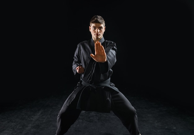Mannelijke karateka, vechtersoefening in zwarte kimono, gevechtshouding. Man op training, vechtsporten, training voordat de concurrentie wordt bestreden