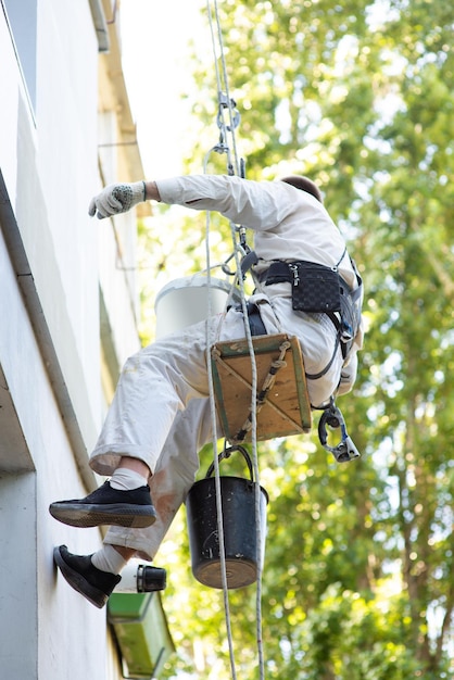 Foto mannelijke klimmer bouwer schildert de gevel van het gebouw