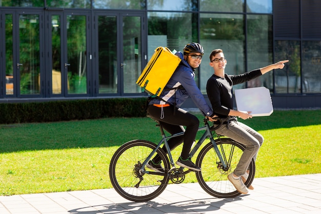 Mannelijke koerier met thermische tas draagt een man met een doos op een fiets kofferbak.