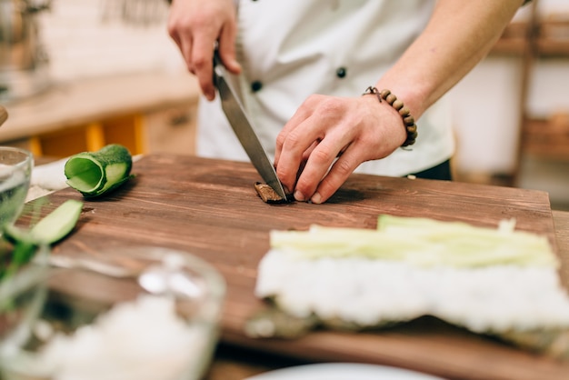 Mannelijke kok sushi rollen maken op houten tafel