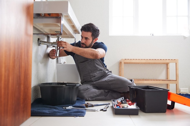 Mannelijke loodgieter bezig met het repareren van lekkende gootsteen in de badkamer thuis