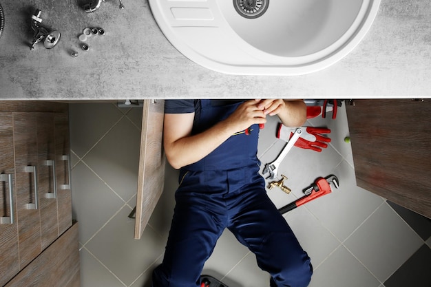 Foto mannelijke loodgieter repareert gootsteenpijpen in bovenaanzicht keuken