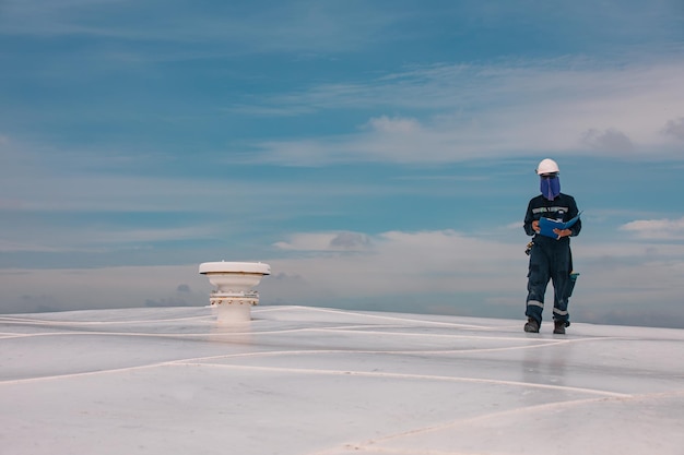 Mannelijke lopende daktankinspectie visuele mondstuk open ventilatieopening op het tankdak witte top blauwe hemel