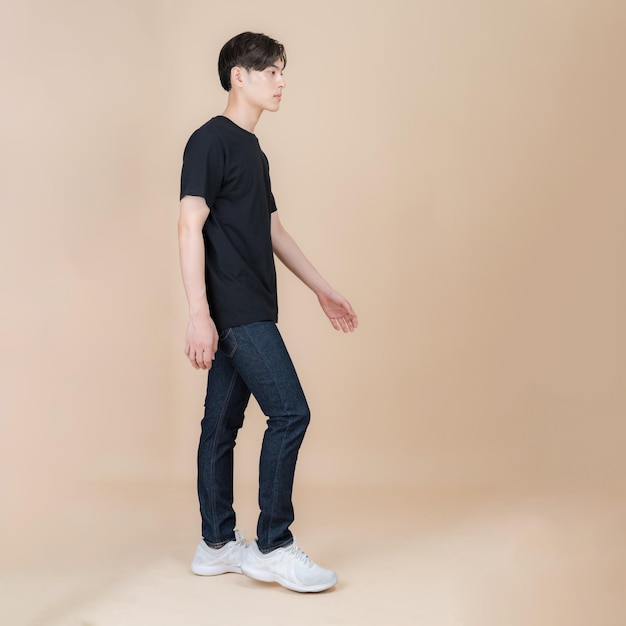 Mannelijke mannequin in zwarte t-shirt en jeans die zich in studio op beige achtergrond bevinden