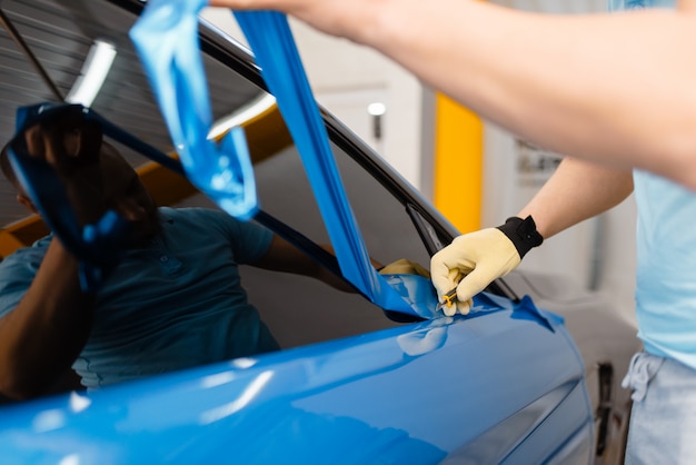 Mannelijke monteur handen installeert beschermende vinylfolie of film op autodeur. Werknemer maakt automatische detaillering. Autolakbescherming, professionele afstemming