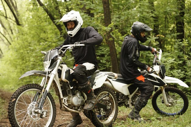 Mannelijke motorrijders in helmen zittend op motoren en voorbereiden om te draaien in bos