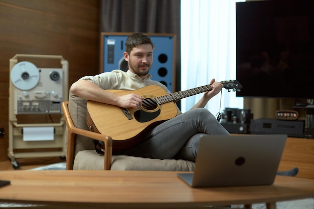 Mannelijke muzikant speelt akoestische gitaar en voert online les uit op laptop Man zanger componist voert muziek uit kijk op computer