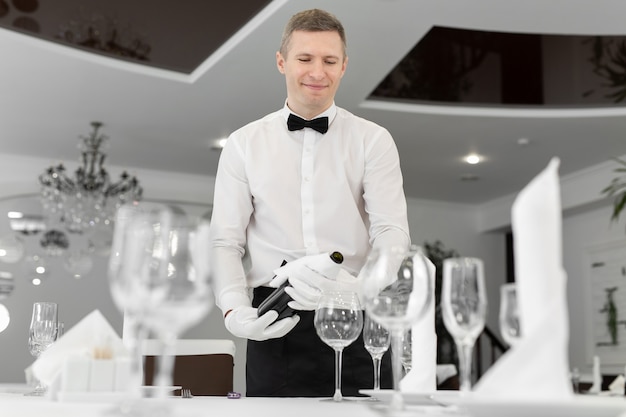 Mannelijke ober in witte handschoenen giet rode wijn in een glas.