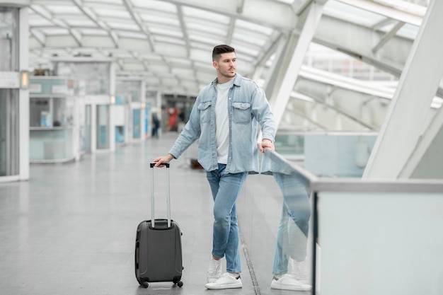 Mannelijke passagier die met reiskoffer op vlucht in luchthaven wacht