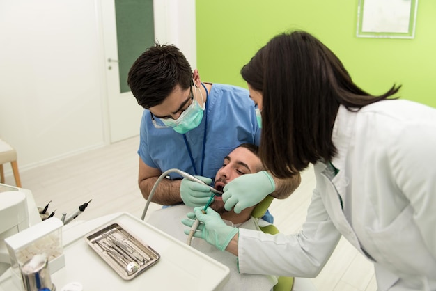 Mannelijke patiënt met tandarts en assistent in een tandheelkundige behandeling met maskers en handschoenen