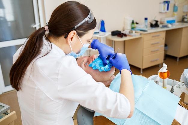 Mannelijke patiënt zit op de stoel van de tandarts en krijgt tandenrestauratie, vrouwelijke tandarts in de tandheelkundige kliniek. Selectieve focus