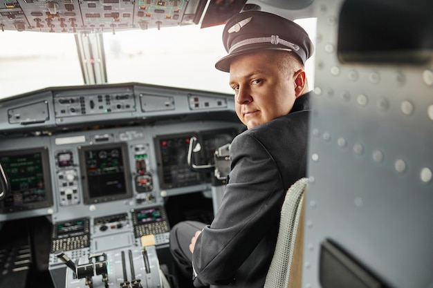 Mannelijke piloot in cockpit van passagiersvliegtuig. Modern vliegtuig met dashboard en luchtvaartnavigatie. Europese man draagt uniform en kijkt naar de camera. Civiele commerciële luchtvaart. Vliegreisconcept