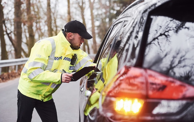 Mannelijke politieagent in groen uniform die voertuig op de weg controleert.