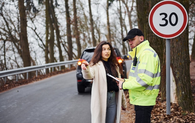 Mannelijke politieagent in groen uniform praten met vrouwelijke eigenaar van de auto op de weg.