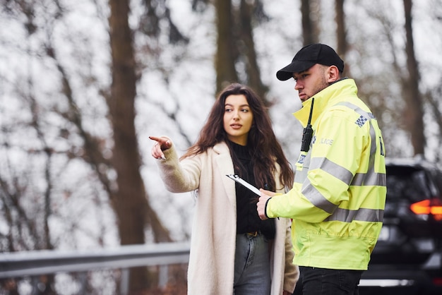 Mannelijke politieagent in groen uniform praten met vrouwelijke eigenaar van de auto op de weg.