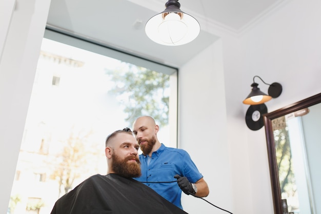 Mannelijke professionele kapper die cliënt door clipper bedient