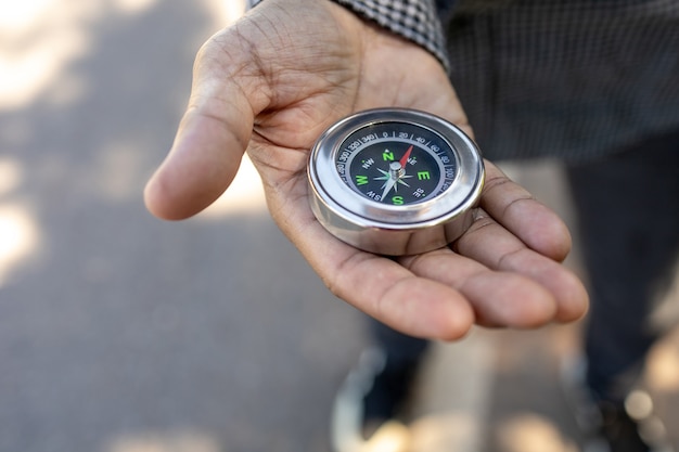 Mannelijke reiziger met een magnetisch kompas op asfaltweg, oriëntatie en je weg vinden.
