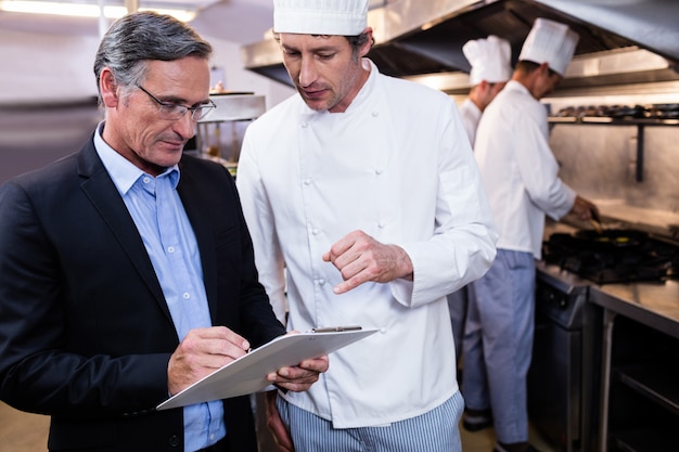 Mannelijke restaurantmanager die op klembord schrijft terwijl het interactie aangaan met chef-kok