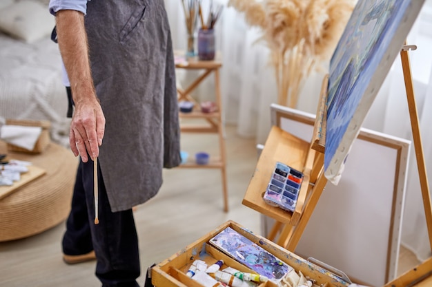 Mannelijke schilder man in schort tijdens het werkproces, man met behulp van verfborstels, verschillende materialen schildert tools om te schilderen