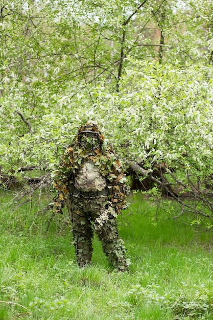 Mannelijke sluipschutter poseren in groene camouflage camouflage kleding in het bos in de buurt van de kersenbloesem. Leger, leger, airsoft, hobbyconcept