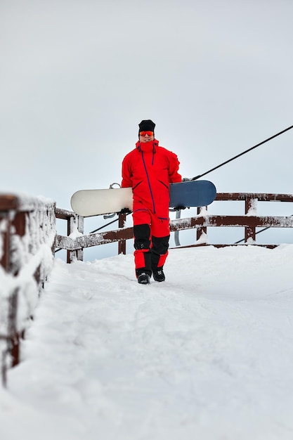 Mannelijke snowboarder in een rood pak lopen op de besneeuwde heuvel met snowboard, skiën en snowboarden concept.