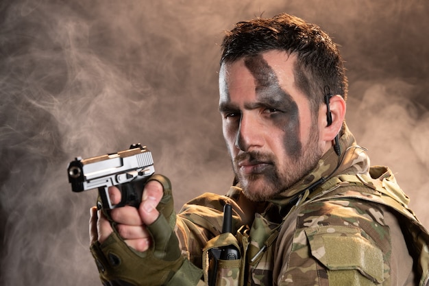 Foto mannelijke soldaat in camouflage die een pistool op de rokerige donkere muur richt