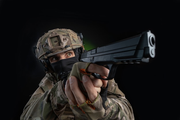 Mannelijke soldaat in militaire jurk met wapen op donkere achtergrond geïsoleerd op zwart gefilmd op groothoek