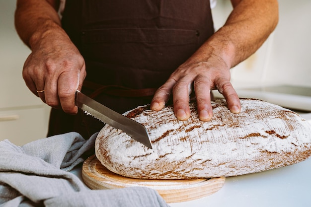 Mannelijke sterke gespierde handen van bakker, in meel, gesneden ambachtelijk zelfgebakken brood van roggemeel