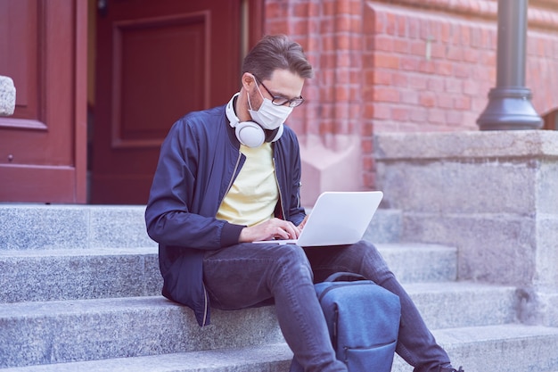 Mannelijke student die op de campus rondhangt met een beschermend masker vanwege de pandemie van het coronavirus