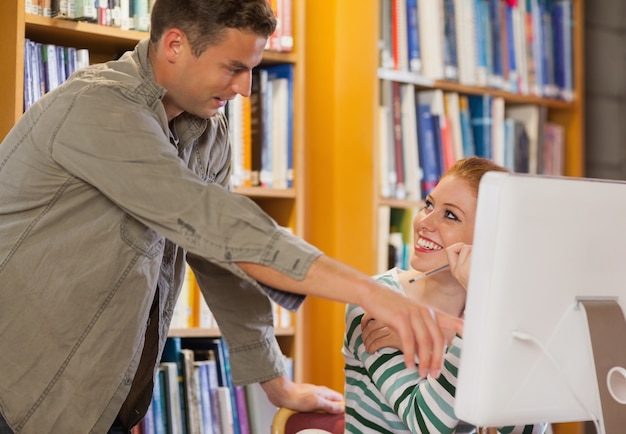 Mannelijke student die zijn klasgenoot iets op de computer verklaart