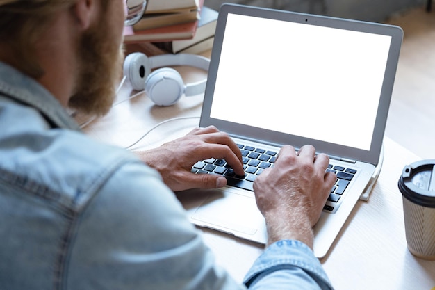 Mannelijke student met behulp van laptop kijken naar witte mock-up scherm over schouder weergave