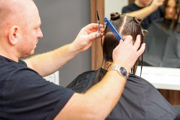 Mannelijke stylist die het haar van een vrouwelijke cliënt in professionele schoonheidssalon knipt